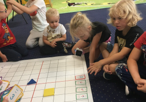 Dzieci siedzą na dywanie i programują genibota.