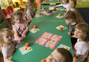 Dzieci siedzą przy stole, a przed nimi leży słodki poczęstunek.