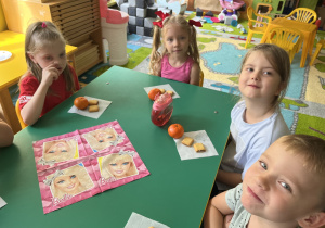 Dzieci siedzą przy stole, a przed nimi leży słodki poczęstunek.