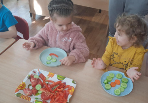 Dzieci siedzą przy stole na których stoją talerze z warzywami.