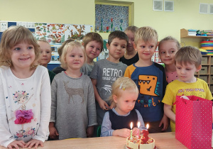 dziewczynka świętuje urodziny, dzieci stoją dookoła niej i składają jej życzenia