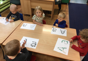 Dzieci siedzą przy stole, a przed nimi leżą karty pracy.