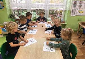 Dzieci siedzą przy stole, a przed nimi leżą karty pracy.