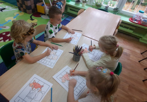 Dzieci siedzą przy stole, a przed nimi leżą karty pracy.