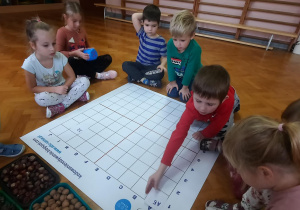 Dzieci siedzą na podłodze i wykonują zadanie na macie do kodowania..