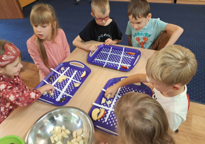 Dzieci siedzą przy stoliku i wykonują owocowe sudoku.
