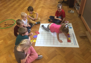 Dzieci siedzą na podłodze i wykonują zadanie na macie do kodowania.