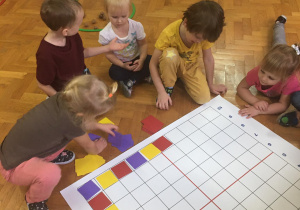 Dzieci siedzą na podłodze i wykonują zadanie na macie do kodowania.