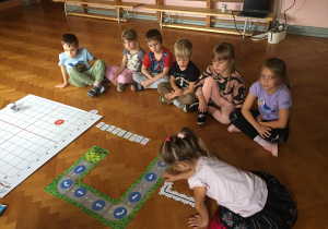 Dzieci siedzą na podłodze i układają drogę dla ozobota z puzzli.