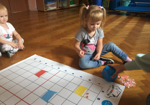 Dzieci siedzą na podłodze i wykonują zadanie na macie do kodowania.