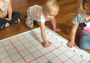 Dzieci siedzą na podłodze i wykonują zadanie na macie do kodowania.