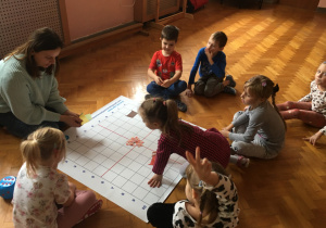 Dzieci siedzą na podłodze i wykonują zadanie na macie do kodowania.
