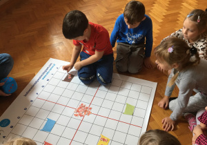 Dzieci siedzą na podłodze i wykonują zadanie na macie do kodowania.