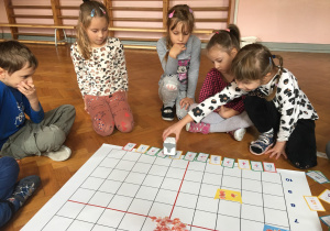 Dzieci siedzą na podłodze i wykonują zadanie na macie do kodowania.