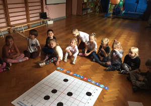Dzieci siedzą na podłodze i wykonują zadanie na macie do kodowania.