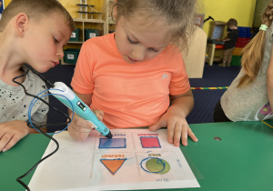 Dzieci siedzą przy stole i rysują figury geometryczne długopisem 3D.