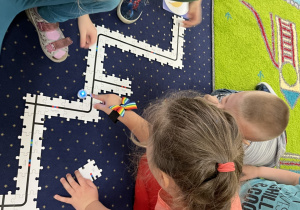 Dzieci siedzą na dywanie i układają drogę z puzzli dla ozobota.