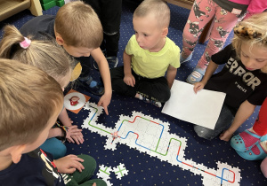 Dzieci siedzą na dywanie i układają drogę z puzzli dla ozobota.