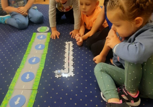Dzieci siedzą na dywanie i wykonują z puzzli drogę dla ozobota.