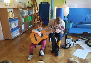 chłopiec trzyma gitarę, starszy chłopiec pokazuje jak prawidłowo chwytać gitarę i na niej grać