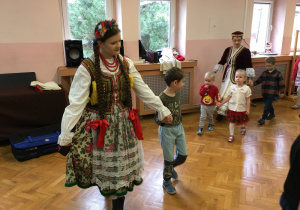 dzieci na sali gimnastycznej tańczą poloneza wraz z osobami ubranymi w stroje ludowe