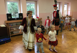 dzieci na sali gimnastycznej tańczą poloneza wraz z osobami ubranymi w stroje ludowe