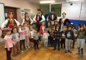 grupa dzieci pozuje do zdjęcia, za nimi widać grupę osób ubranych w stroje krakowskie i szlacheckie
