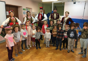 grupa dzieci pozuje do zdjęcia, za nimi widać grupę osób ubranych w stroje krakowskie i szlacheckie