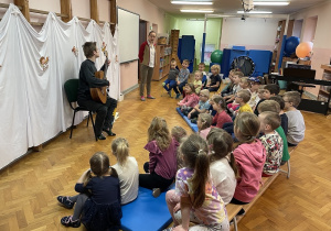 koncert gitarowy na sali gimnastycznej, dzieci siedzą na krzesełkach, chłopiec gra na gitarze