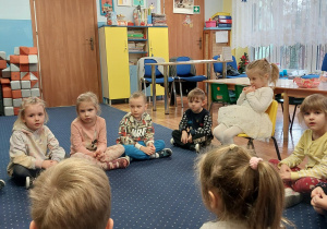 dziewczynka siedzi na krześle, dookoła niej siedzą dzieci na podłodze w klasie