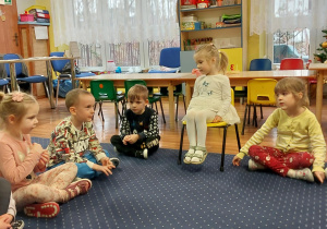 dziewczynka siedzi na krześle, dookoła niej siedzą dzieci na podłodze w klasie
