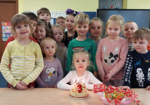 dziewczynka świętuje urodziny, dzieci z jej grupy stoją za nią, na stoliku widać symboliczny tort