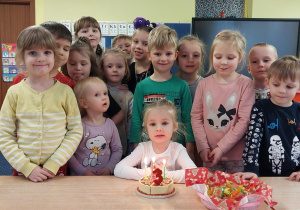 dziewczynka świętuje urodziny, dzieci z jej grupy stoją za nią, na stoliku widać symboliczny tort