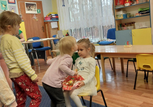 dziewczynka siedzi na krześle, dzieci z grupy składają jej urodzinowe życzenia