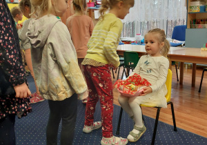 dziewczynka siedzi na krześle, dzieci z grupy składają jej urodzinowe życzenia
