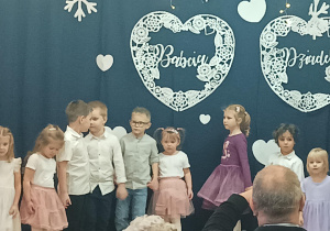 dzieci z grupy 2 występują na sali gimnastycznej, w tle dekoracja z napisami babcia i dziadek