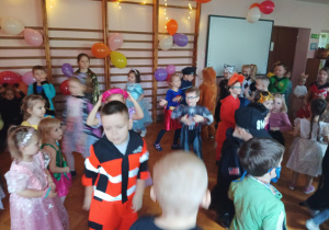 dzieci w przebraniach karnawałowych tańczą na balu przebierańców, na sali gimnastycznej