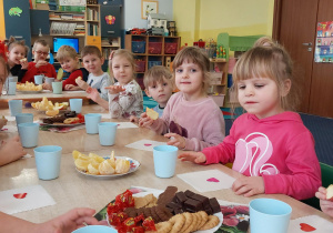 dzieci siedzą przy stolikach, na których są słodycze, napoje