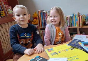 chłopiec z dziewczynką oglądają książki przy stoliku w bibliotece