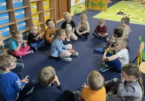 dzieci siedzą w kręgu na podłodze w sali, po środku sziedzi dziewczynka