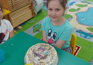 Dziewczynka siedzi przy stole, przed nią znajduje się tort.