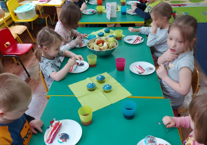 Dzieci siedzą przy stole i zjadają tort.