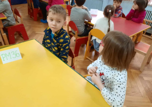 Dzieci siedzą przy stolikach.