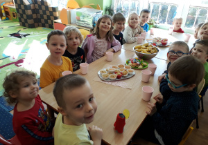 Wszystkie dzieci siedzą przy stole na którym stoi słodki poczęstunek.