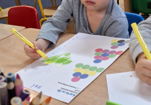 Dzieci siedzą przy stoliku i wykonują zadanie z kodowania.
