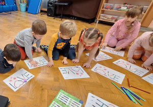 Dzieci siedzą na podłodze, przed nimi leżą kartki z napisem "LOVE".