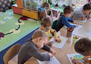 Dzieci siedzą przy stolikach i kolorują obrazki.