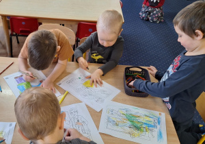 Dzieci siedzą przy stolikach i kolorują obrazki.
