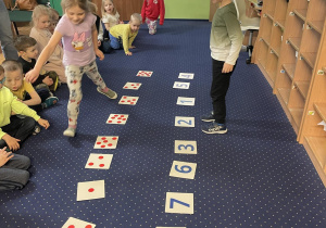Dzieci siedzą na dywanie, dwoje z nich wykonuje zadanie matematyczne.