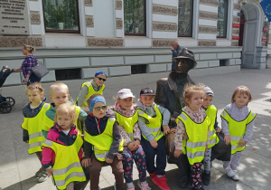 grupa dzieci w żółtych kamizelkach pozują do zdjęcia na ul. Piotrkowskiej na ławeczce Juliana Tuwima